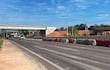 Dos vehículos en movimiento en carretera, sin personas visibles, bajo un cielo despejado y con obras en construcción al fondo.