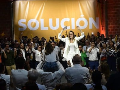 Soledad Núñez de pie levantando los brazos, rodeada de seguidores aplaudiendo y agitando pañuelos amarillos en un ambiente festivo.