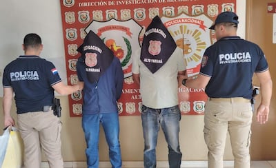 Dos hombres con pañuelos negros en la cara son detenidos por un agente de policía en una comisaría.