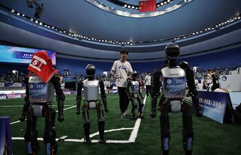 Robots humanoides y técnicos abandonan un campo de fútbol 5 contra 5 tras un partido durante los Juegos Mundiales de Robots Humanoides 2025 en el Óvalo Nacional de Patinaje de Velocidad en Pekín, China, el 17 de agosto de 2025.