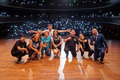 Ocho comediantes muestran sonrisas y gestos de celebración en un escenario iluminado, rodeados de luces de teléfonos móviles del público.
