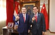 Cartes y Baruja sonríen, ambos en trajes oscuros y corbatas rojas, en un despacho adornado con banderas.