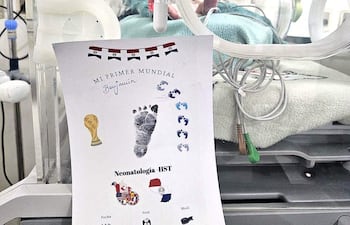 Recién nacido en incubadora con documentos que celebran su primer Mundial, destacando huellas y gráficos relacionados con el fútbol.