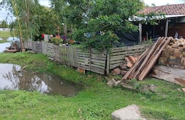 Entorno rural con agua estancada, cercado de madera y césped, sin personas visibles.