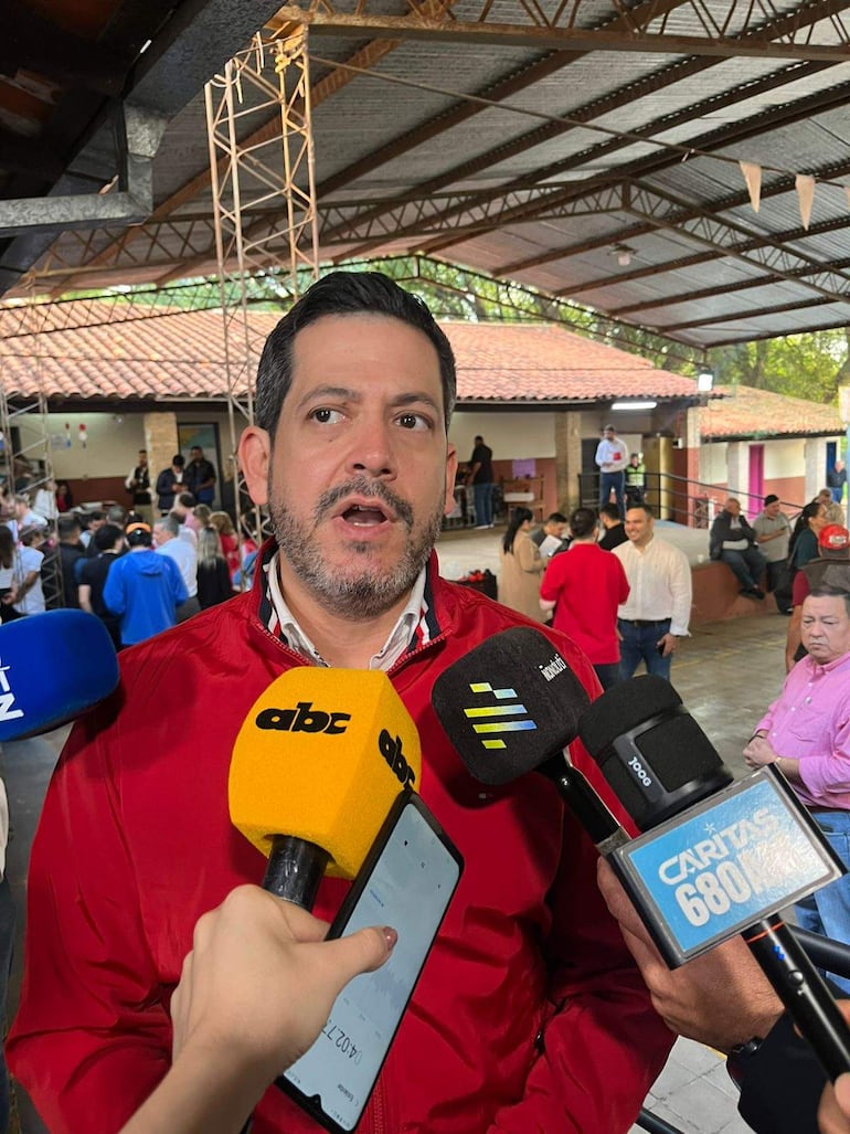 Raúl Latorre Martínez con chaqueta roja hablando a micrófonos, rodeado de periodistas y miembros de la audiencia atentos.