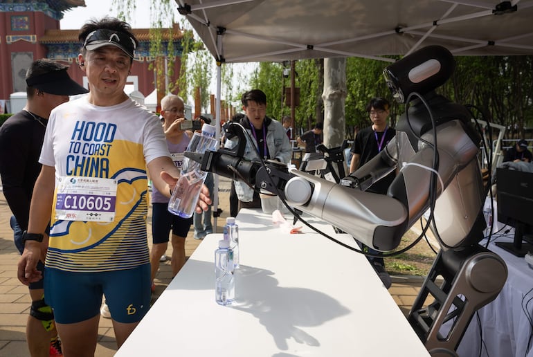 Un robot humanoide le entrega una botella de agua a un corredor durante la segunda Beijing E-Town Half Marathon and Humanoid Robot Half Marathon, una media maratón disputada por humanos y robots humanoides, en Beijing, China, el 19 de abril de 2026.