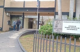 Tres personas en la entrada del juzgado, conversando, rodeadas de un entorno urbano con naturaleza.