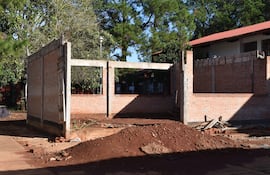 Construcción de aulas en mal estado con paredes de ladrillo y escombros en terreno desordenado, sin actividad visible.