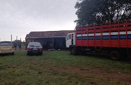 Cuatro personas conversan junto a vehículos en un entorno rural, con una casa de campo al fondo y cielos nublados.