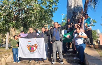 Grupo de diez personas en protesta, algunos con pancartas y banderas, expresiones de determinación y apoyo entre los asistentes.