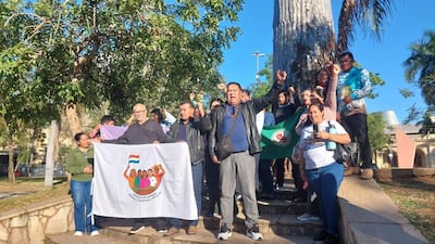 Grupo de diez personas en protesta, algunos con pancartas y banderas, expresiones de determinación y apoyo entre los asistentes.