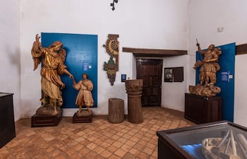 Esculturas de un ángel, un niño y un guerrero en una sala tranquila con paredes blancas y azules.