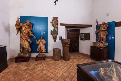 Esculturas de un ángel, un niño y un guerrero en una sala tranquila con paredes blancas y azules.