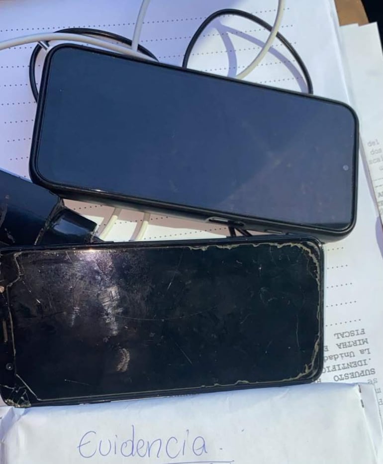 Dos teléfonos móviles sobre papel, uno negro intacto y otro dañado, conectados por cables, con la palabra 'Evidencia'.