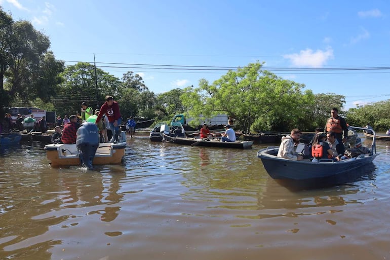 Hombres en botes y orilla, algunos con abrigo claro, en un entorno inundado bajo un cielo despejado.
