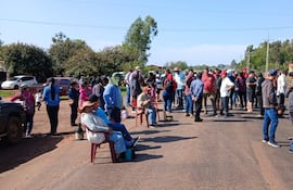 Grupo de personas en pie y sentadas conversando, con ropa casual y un entorno de casas y vegetación.