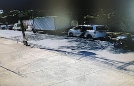 Escena urbana con vehículos estacionados, destaca un camión blanco y autos de diferentes colores en un ambiente cotidiano.