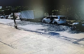 Escena urbana con vehículos estacionados, destaca un camión blanco y autos de diferentes colores en un ambiente cotidiano.