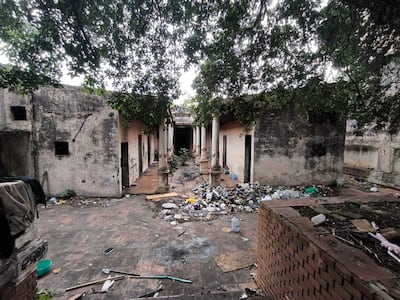 Patio abandonado con paredes de adobe, suelos desgastados y basura acumulada, rodeado de vegetación.