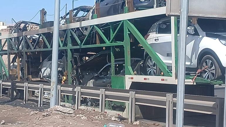 Camión transportador de automóviles en llamas, con vehículos asegurados en la plataforma elevada, ambiente despejado.