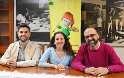 Claudio Pusineri con chaqueta clara, Pili Ortiz en blusa azul y Roberto Galeano Monti en suéter rosado, sonriendo alrededor de una mesa.