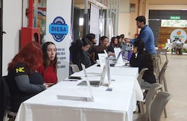 Mujer de cabello largo y rojo conversando en un ambiente interior, con mesas blancas y documentos sobre la mesa.