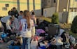 Niña con camiseta de Paraguay y número 10, rodeada de mujeres que organizan pertenencias en un ambiente de asistencia humanitaria.