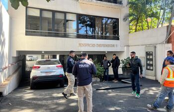 Ocho hombres en la entrada del Edificio Defensor 1, con dos policías conversando y uno de ellos en chaleco amarillo.