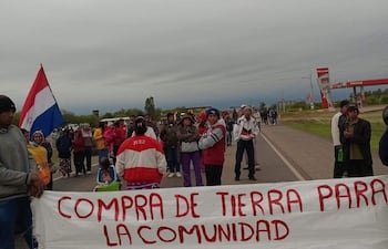 Hombres y mujeres de la comunidad Tooshe Qáltaq sosteniendo un banner con la inscripción ‘COMPRA DE TIERRA PARA LA COMUNIDAD TOOSHE QALTAQ’.