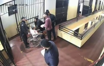 Hugo Javier en silla de ruedas, ensangrentado, rodeado por personal de seguridad y un adulto entregándole un objeto.