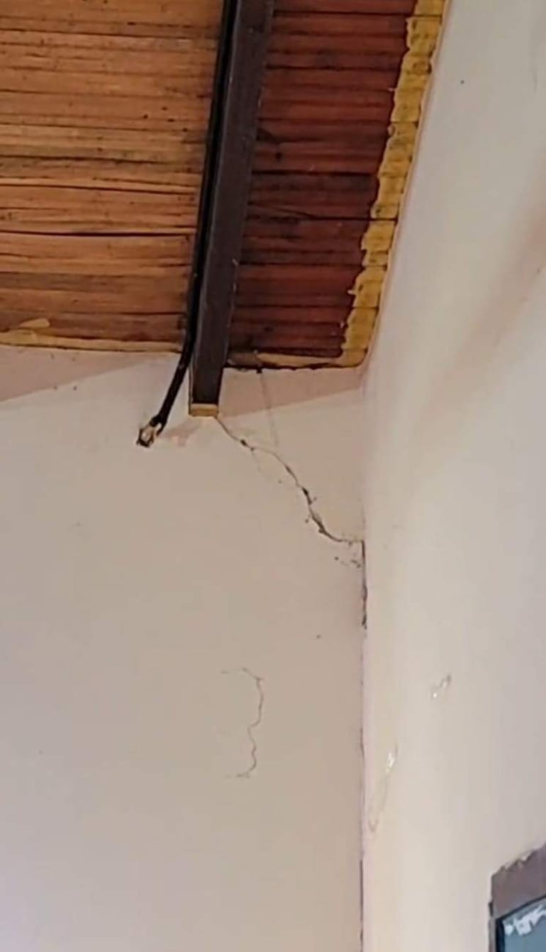 Grieta visible en la pared de una clase con techo de madera, sin personas presentes.