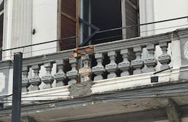 Balcón de edificio antiguo en Asunción, con puertas de madera abiertas y barandilla deteriorada, evidenciando el desgaste del tiempo.