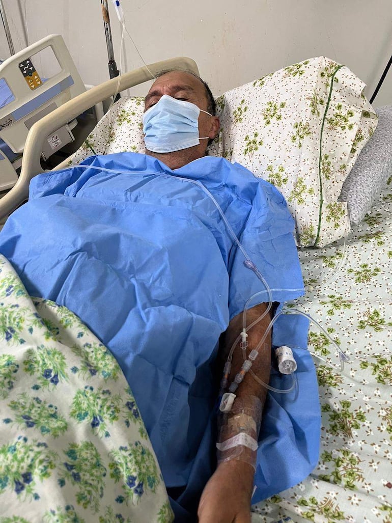 Andrés Alberto Méndez López en cama de hospital con camisa azul y mascarilla, recibiendo atención médica y conectado a dispositivos médicos.
