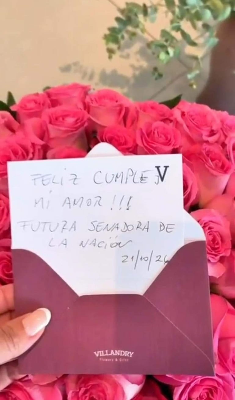 Ramo de rosas rosas con tarjeta blanca que dice 'Feliz cumple mi amor!!!'. Ambiente interior acogedor.