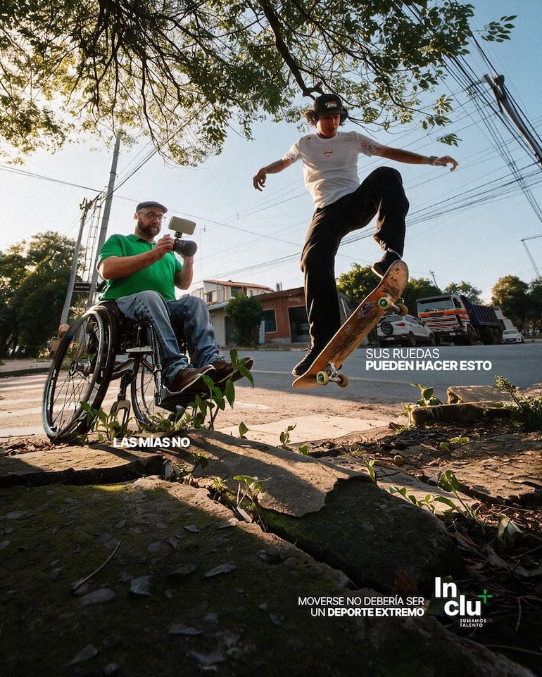 Un hombre en silla de ruedas graba la acción de un patinador que salta, en un entorno urbano con edificios de fondo.
