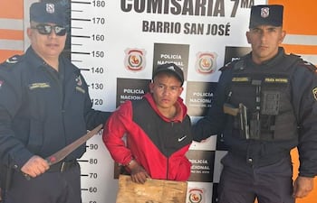 Tres hombres en la comisaría: dos policías con gafas de sol, uno sostiene un machete, el detenido viste camiseta roja y negra, rostro tranquilo.