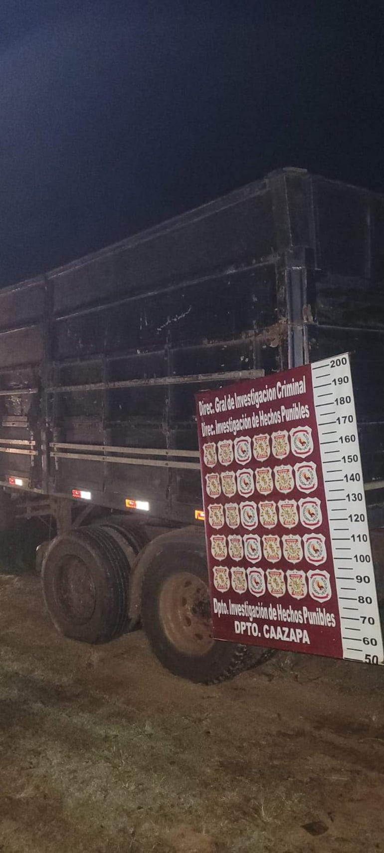 Camión de transporte en un entorno nocturno, junto a un panel informativo con emblemas de instituciones.