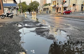 Avenida Ygatimi con baches visibles y un ciclomotor y dos autos en un semáforo, envueltos en un ambiente urbano.