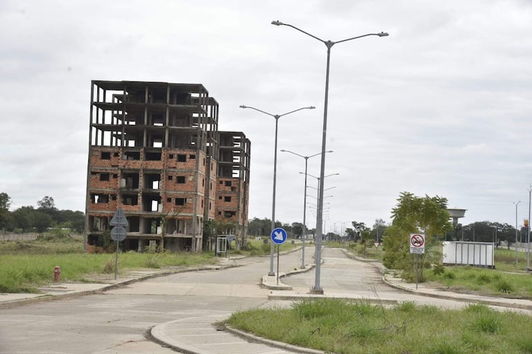 Edificio en ruinas con ladrillos expuestos y vegetación crecida, rodeado de pavimento deteriorado en un día nublado.