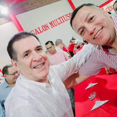 Cubilla en camisa blanca y Cartes en camisa a rayas, sonriendo juntos en un salón decorado con elementos rojos.