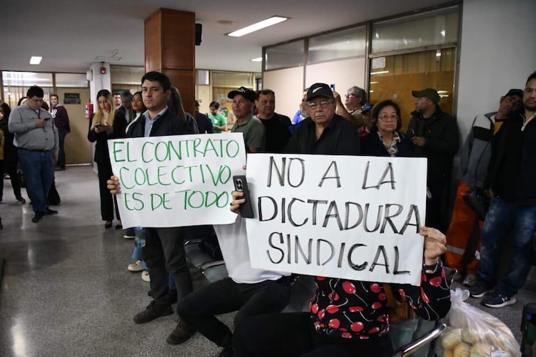 Grupo de personas, algunos con celulares, sostiene carteles que dicen 'EL CONTRATO COLECTIVO ES DE TODO' y 'NO A LA DICTADURA SINDICAL'.