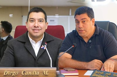 Diego Candia con chaqueta oscura y pin en la solapa se abraza con un hombre de camiseta negra en oficina.