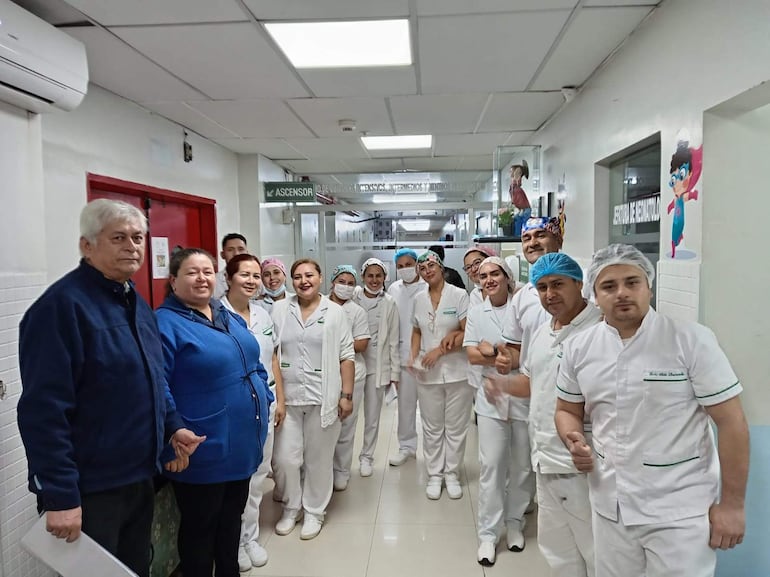 Grupo de enfermeros, principalmente mujeres y hombres con uniformes blancos, sonríen y gesticulan en un pasillo con decoración infantil.