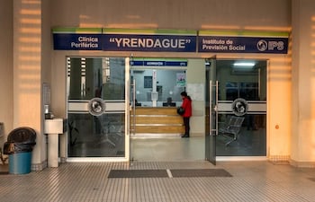 Mujer con abrigo rojo en la entrada de la Clínica Yrendague, situada en un entorno urbano, accediendo al área de admisión.