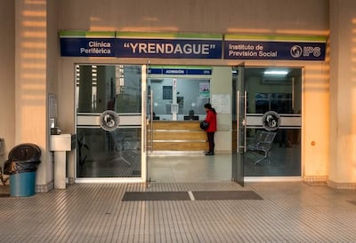 Mujer con abrigo rojo en la entrada de la Clínica Yrendague, situada en un entorno urbano, accediendo al área de admisión.