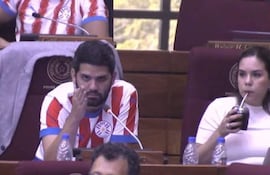 Raúl Benítez con camiseta roja y blanca, Johanna Ortega con camiseta blanca sosteniendo un vaso, en un recinto legislativo.