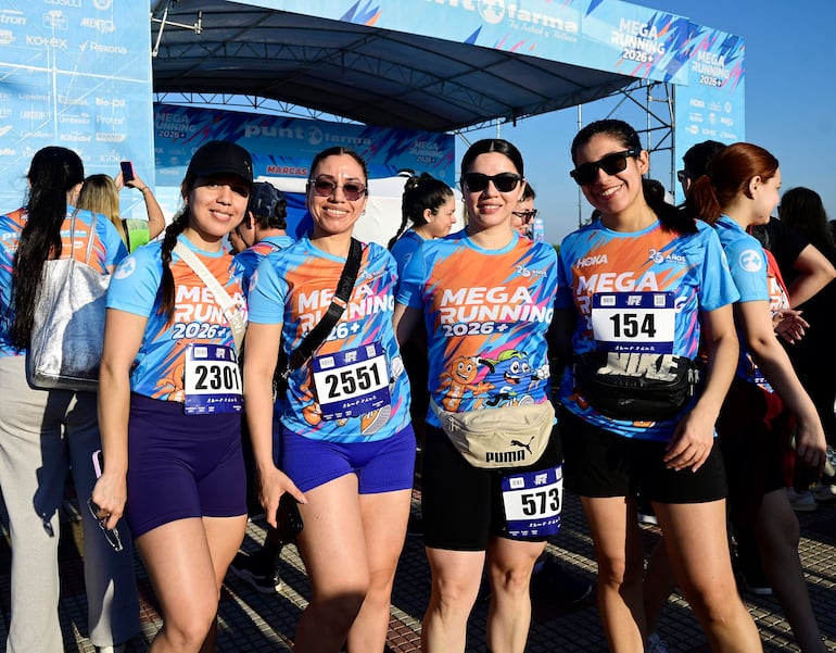 Cuatro mujeres sonrientes en camisetas de running color azul con números, posan en un ambiente al aire libre en un evento deportivo.