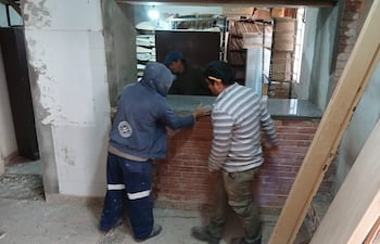 Tres hombres en ambiente de construcción; uno con sudadera, otro en camiseta de rayas, trabajando en encimera de granito.