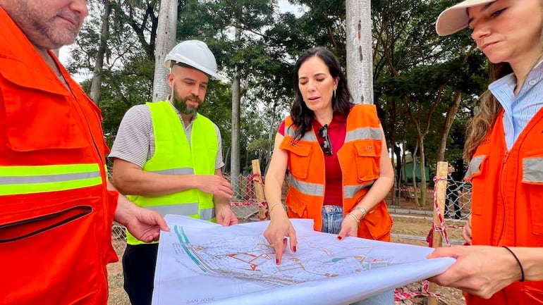 Cuatro trabajadores en chalecos de seguridad analizan planos en un entorno de construcción en Parque Caballero, rodeados de árboles.