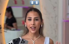 Mujer con cabello largo y lacio, vistiendo blusa blanca, sostiene tres teléfonos móviles mientras sonríe a la cámara.